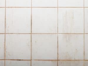 Dirty white bathroom tiles with visible grout stains indicating early signs of shower wall leak urgency.