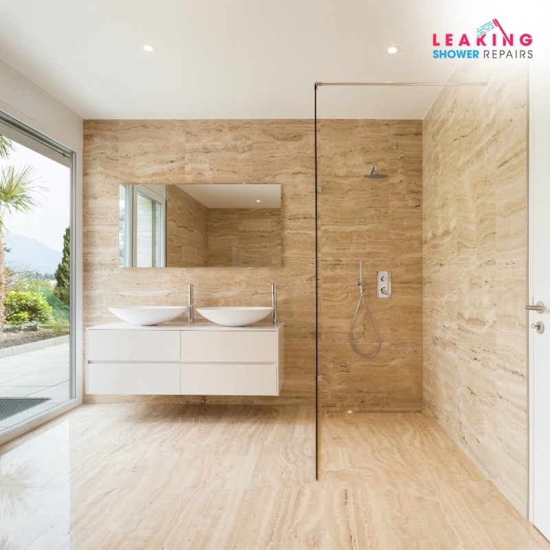 Modern bathroom featuring double vessel sinks, a glass shower, and natural stone walls, with a serene outdoor view, professionally restored through expert leaking shower repairs in Copacabana.